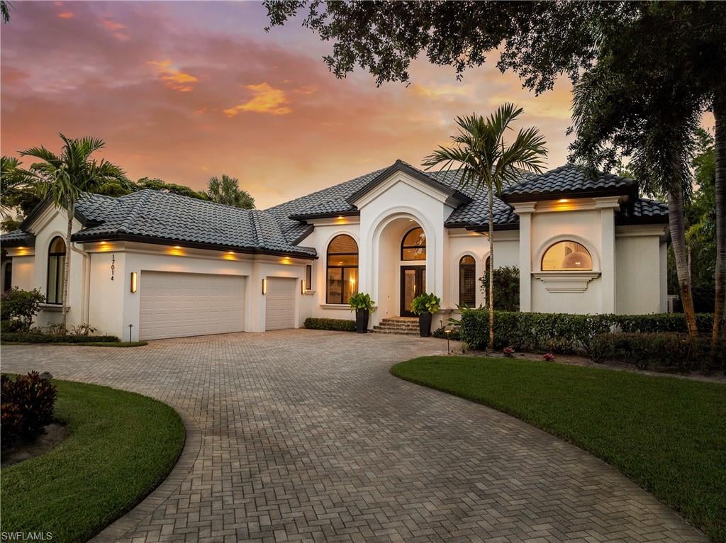 Luxury home in Mediterra Naples, Florida, featuring Mediterranean architecture, a tile roof, and a landscaped brick-paver driveway.