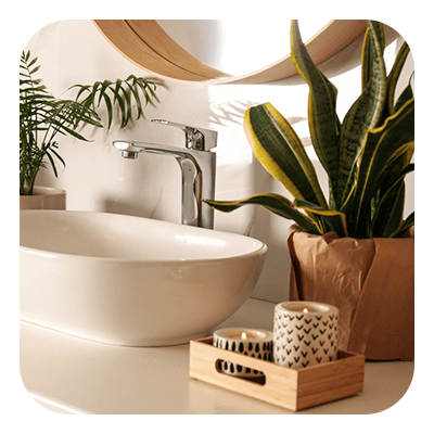 Bathroom vanity with a white vessel sink, chrome faucet, potted plants, and candles on a wooden tray.