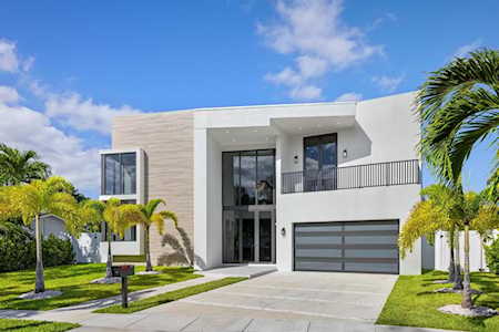 Modern two-story home with a glass-fronted entry, balcony, and palm-lined driveway.