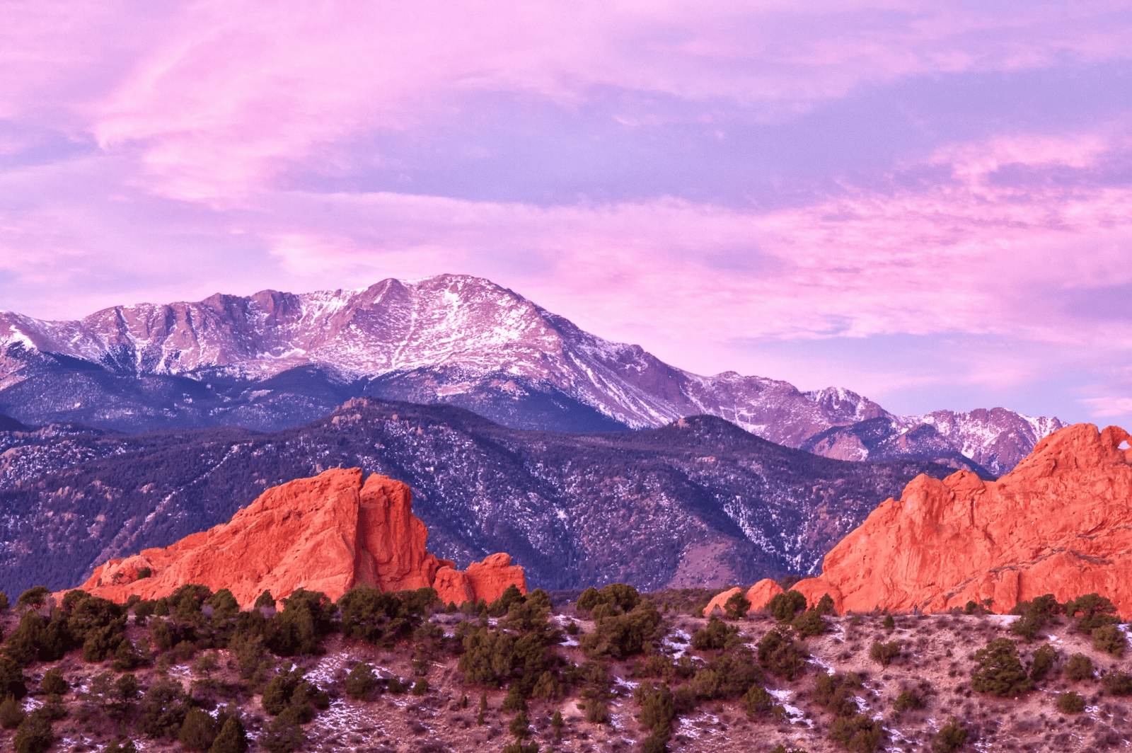 Red sandstone formations frame snow-dusted mountains beneath a pink-purple sky.