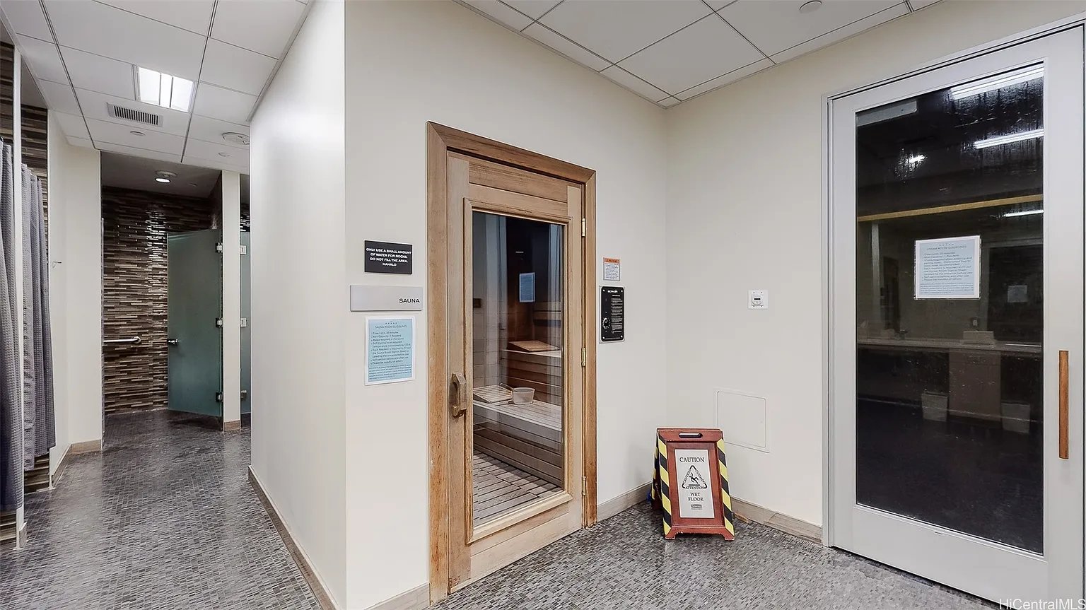 Sauna entrance in a tiled amenity hallway, with glass doors and a wet-floor sign.