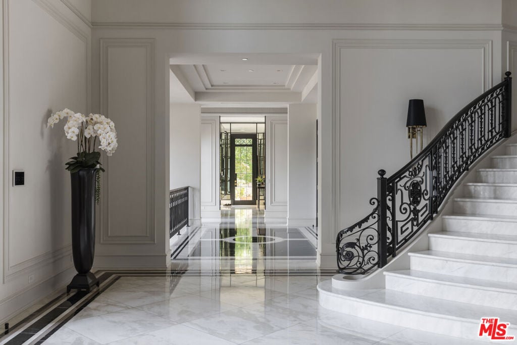 Grand foyer with polished marble floors, a curved staircase, and ornate black railing.