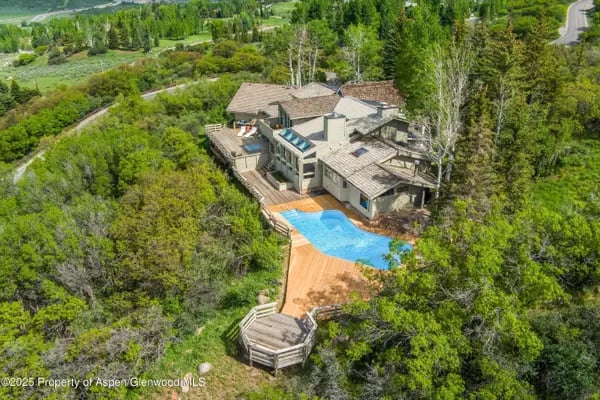 Modern mountain home surrounded by trees, with a blue pool and expansive wood deck.