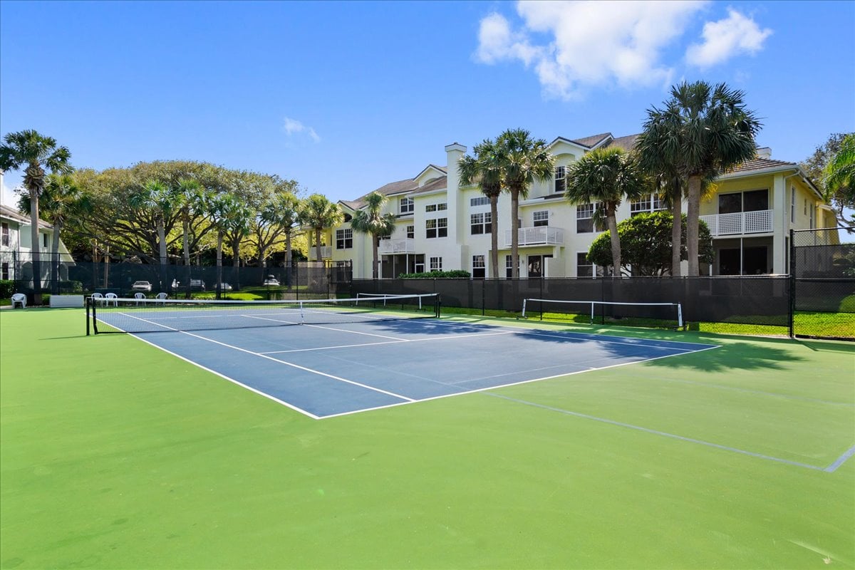 Tennis court at Sea Colony Condominium, with palm trees and the condominium building behind it.