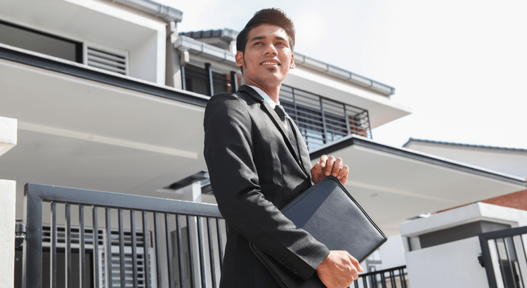 A man in a suit stands in front of a house, holding a folder in his hands, exuding professionalism and readiness.