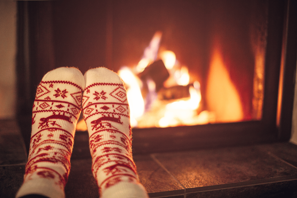 Patterned knit socks point toward a glowing fireplace.