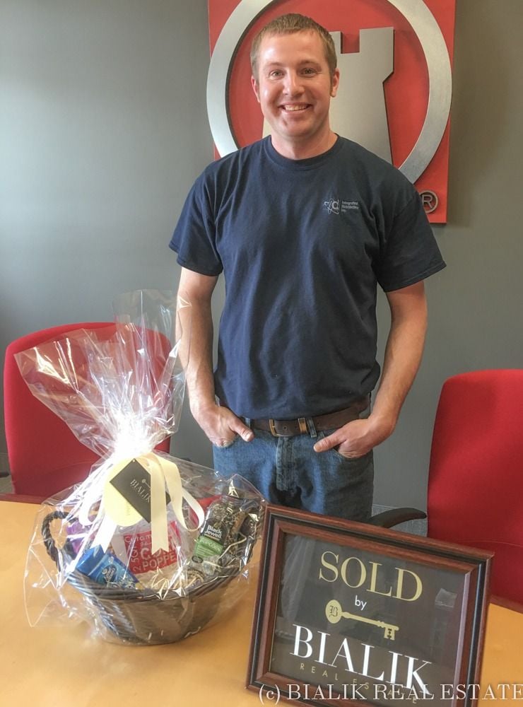 Smiling man beside a gift basket and SOLD by Bialik Real Estate sign.