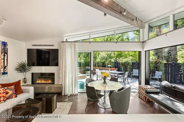 Modern living room with fireplace and television, opening onto a leafy garden patio.
