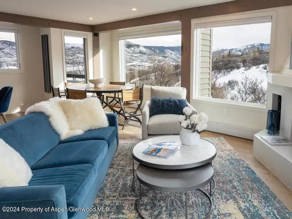 Living room with a blue sofa and large windows overlooking snow-covered mountains.
