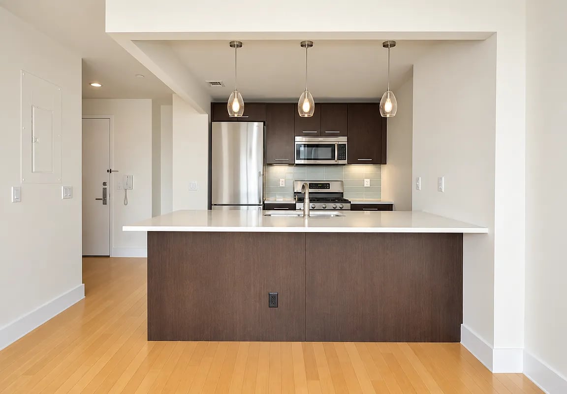 Modern apartment kitchen with a broad dark-wood island, stainless steel appliances, and three pendant lights.