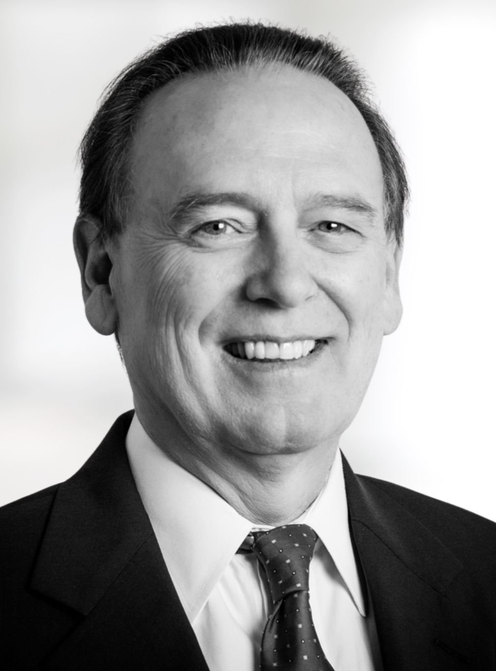 Richard Boote smiling in a black-and-white portrait, wearing a dark suit and patterned tie.