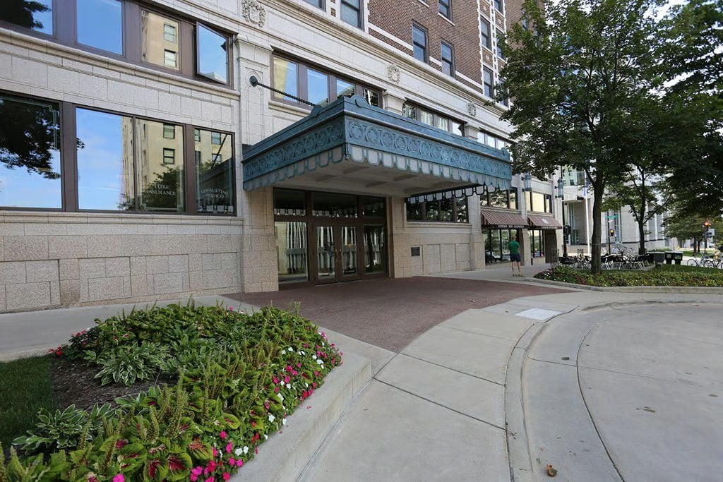 Stone-and-brick building entrance with a blue decorative canopy and flower bed.