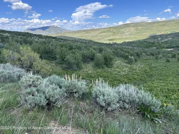 Sagebrush-covered hills and distant mountains beneath a partly cloudy sky.