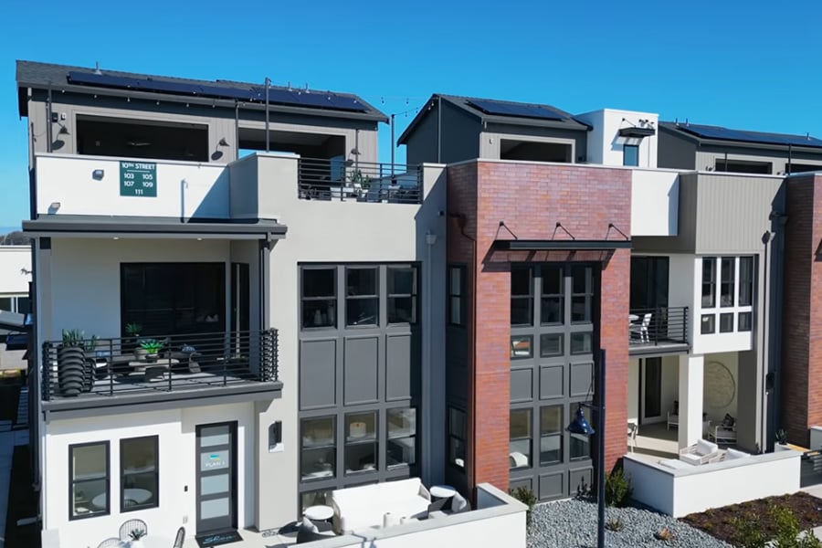 Modern multi-unit building with balconies, red brick accents, rooftop solar panels, and outdoor seating.
