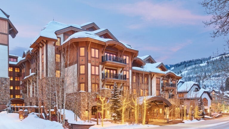 Snow-covered mountain lodge with timber balconies and warmly lit windows at dusk.