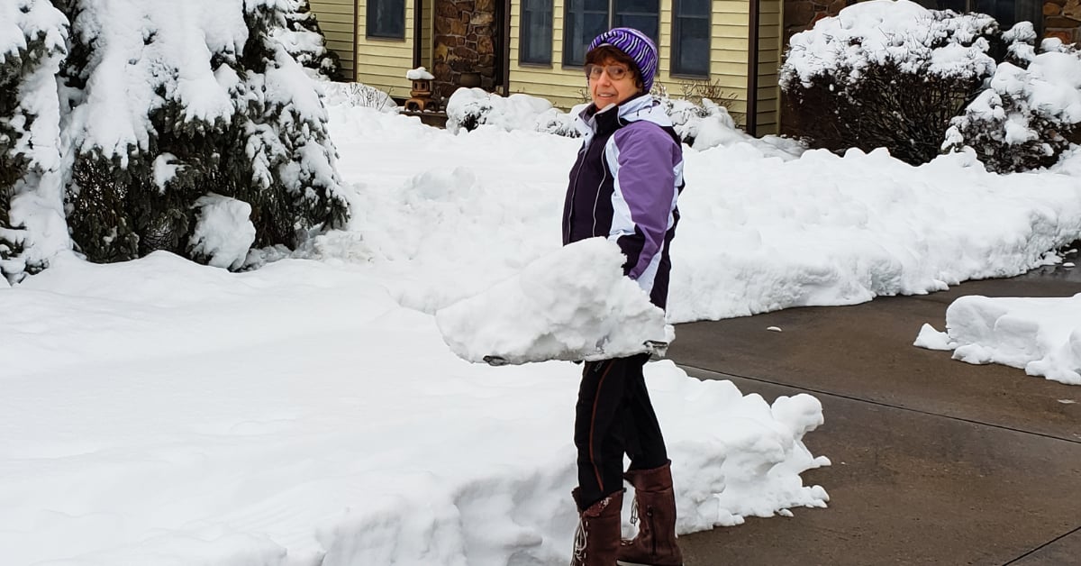 Person shoveling a snowy driveway in front of a home to keep walkways clear and safe for winter showings.