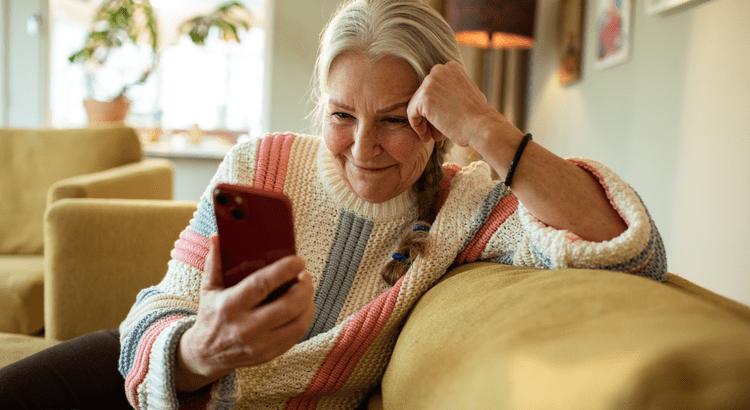 An older woman seated on a couch, intently gazing at her phone, with a thoughtful expression on her face.