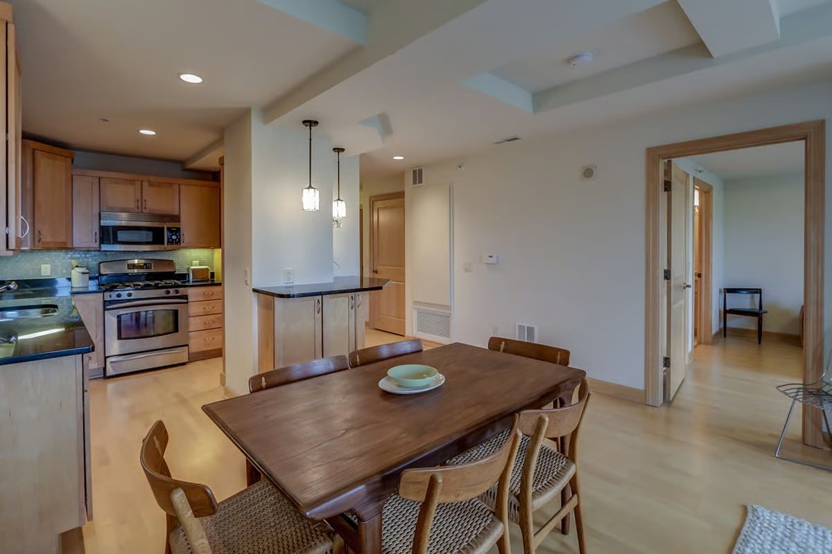 Open-plan kitchen and dining area with wood cabinets, stainless steel appliances, and a large wooden table.