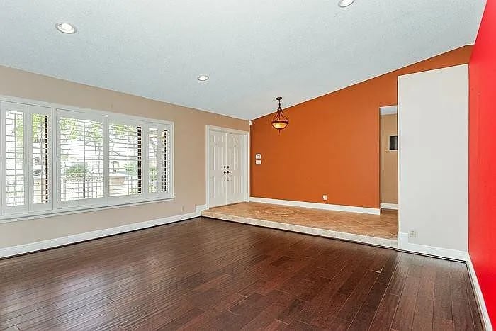 Vacant room with dark wood floors, shuttered windows, and an orange accent wall.