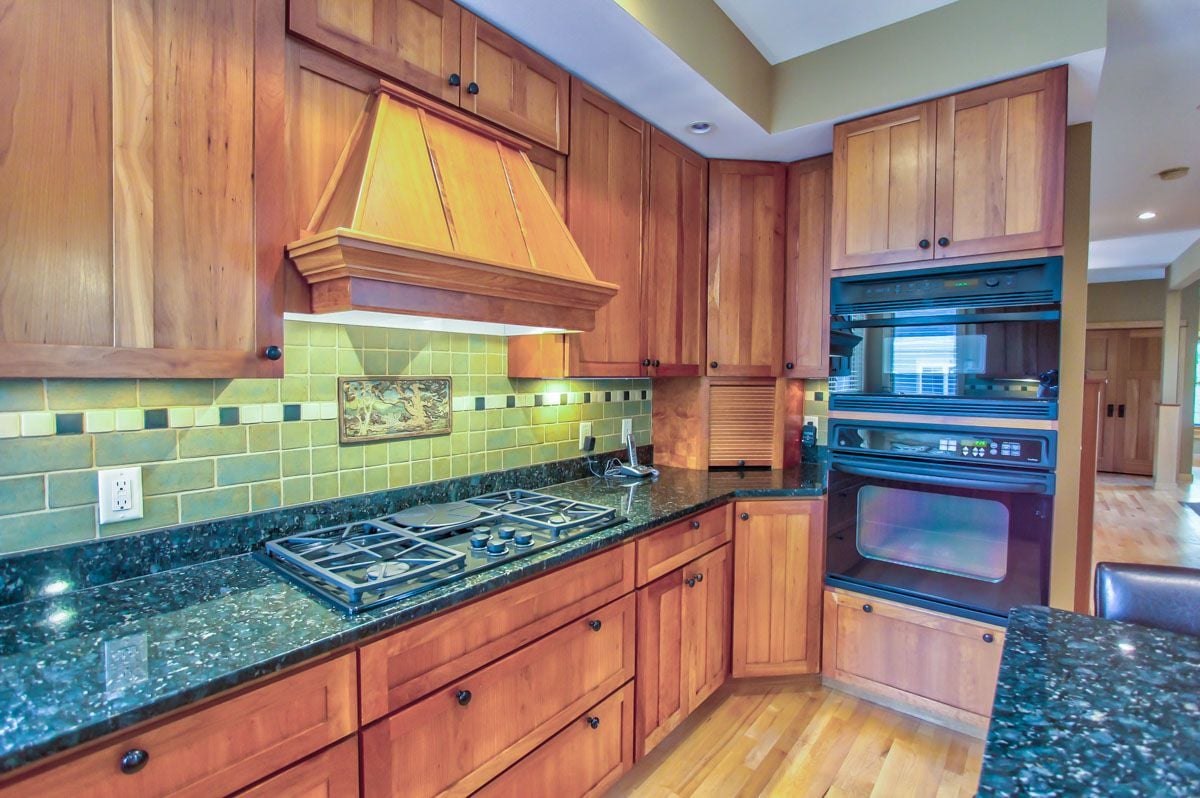 Kitchen with wood cabinetry, granite counters, a gas cooktop, and stacked wall ovens.