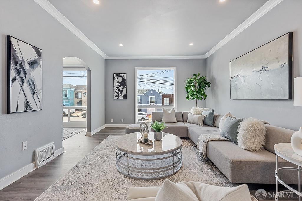 Staged living room with a gray sectional, round coffee table, and large street-facing windows.