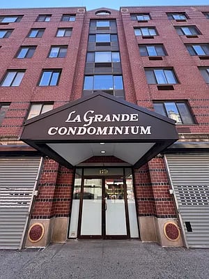 La Grande Condominium entrance beneath a large sign, with a brick façade and central glass windows.