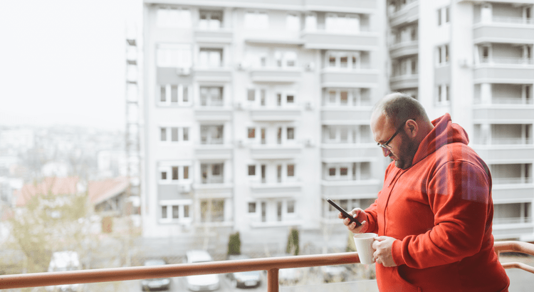 A man in a red hoodie gazes intently at his phone, absorbed in its screen.