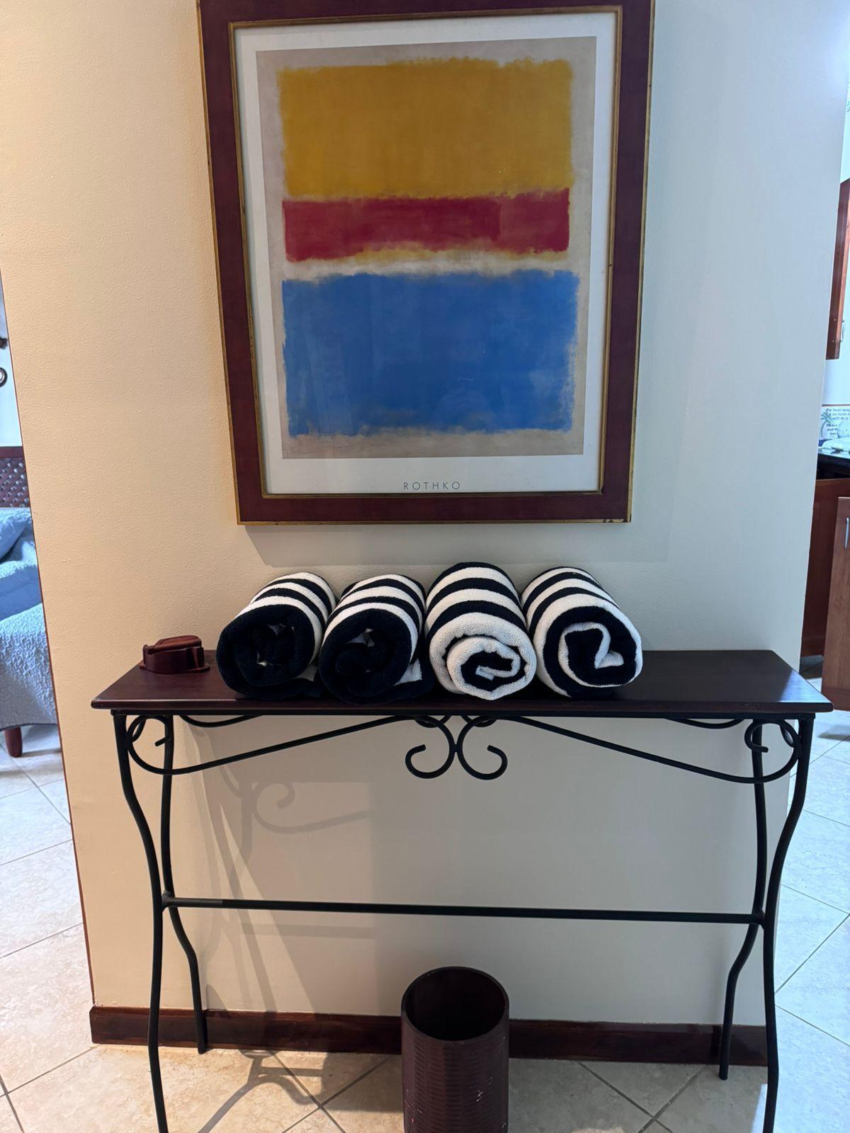 Condo entry console with rolled towels beneath a framed abstract print.