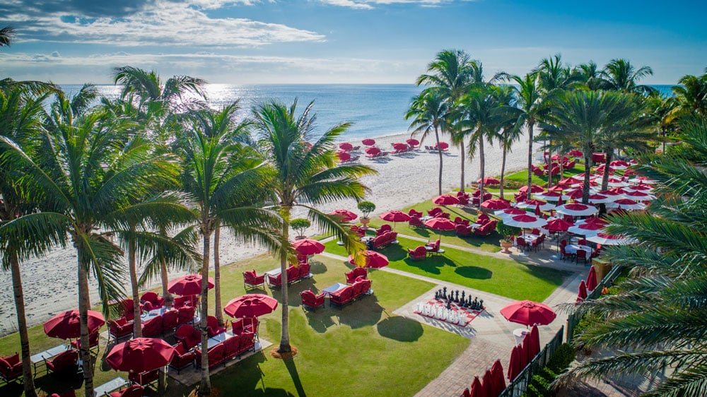 Acqualina beachfront with palm trees, red loungers and umbrellas beside the ocean.