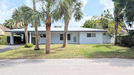 Single-story white house with a covered carport, palm trees, and a front lawn.