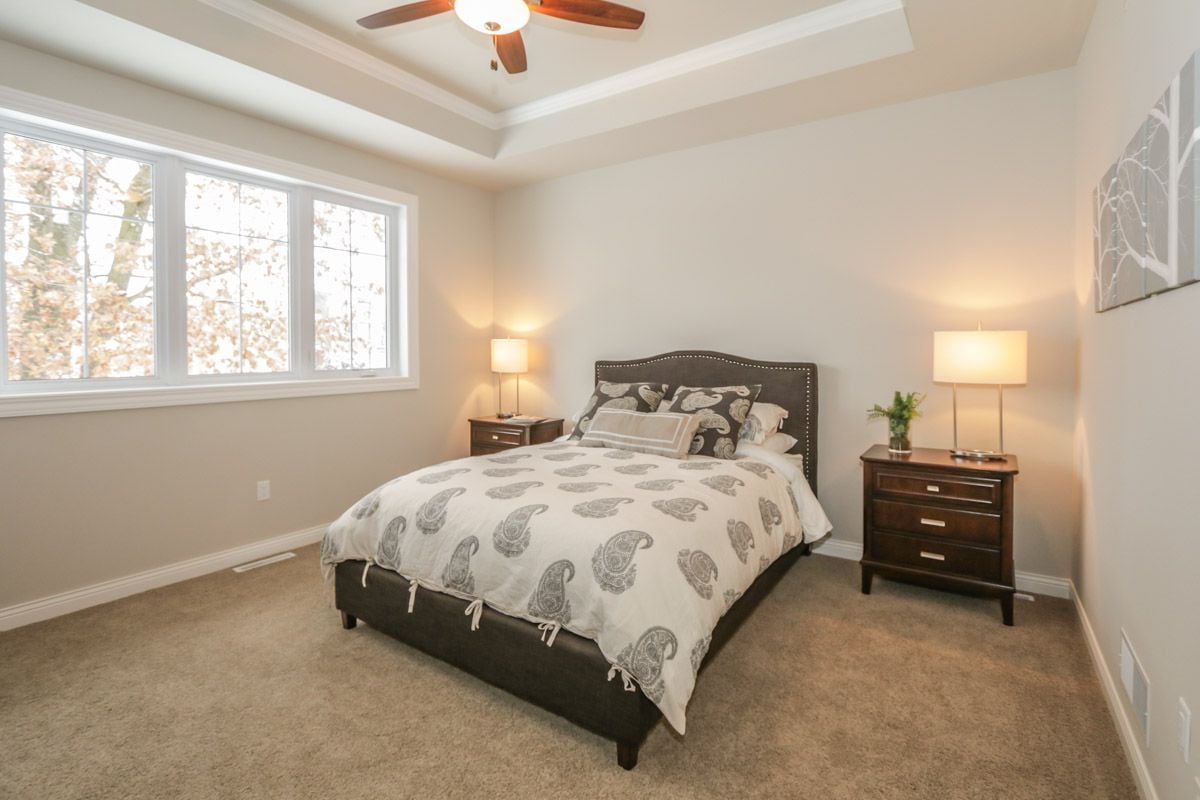 Furnished bedroom with a dark upholstered bed, tray ceiling, and large windows overlooking autumn foliage.
