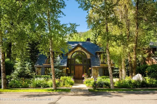 Aspen home with a tall arched entrance, dark roof, and landscaped garden among mature trees.