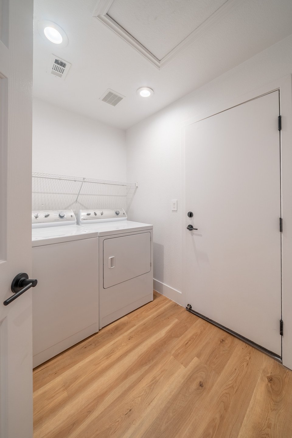 Laundry room with a washer and dryer, wire shelving, and light wood flooring.