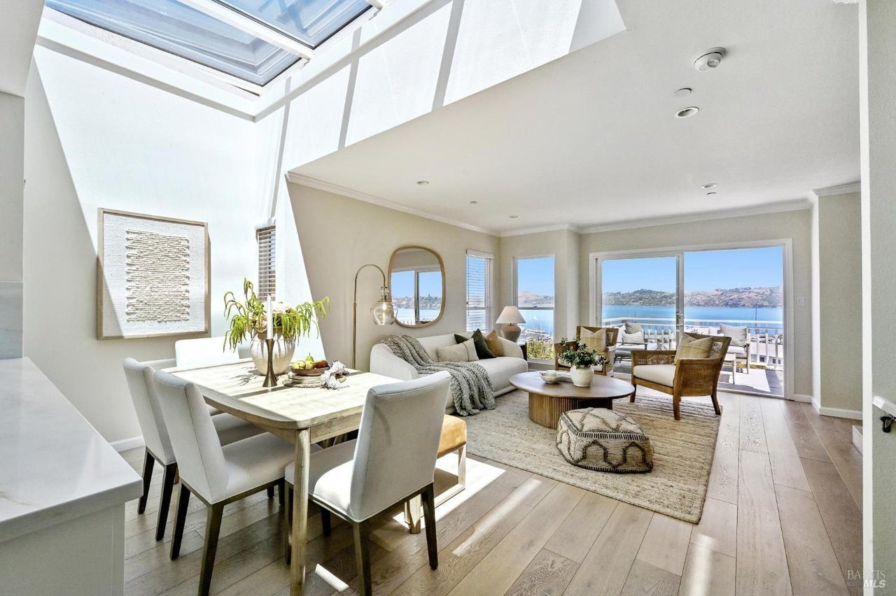 Open-plan living and dining room with a large skylight and water views through glass doors.