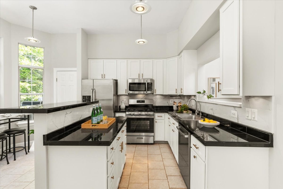 Bright kitchen with white cabinets, black countertops, and stainless steel appliances.