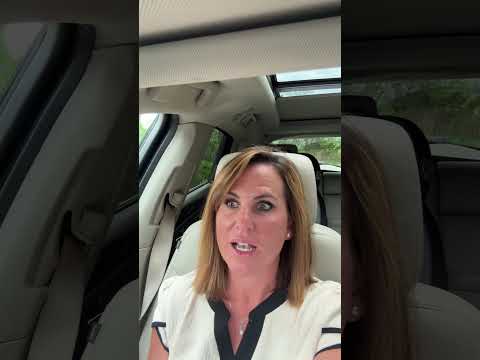 Woman speaking to the camera from a car, wearing a seat belt beneath a sunroof.