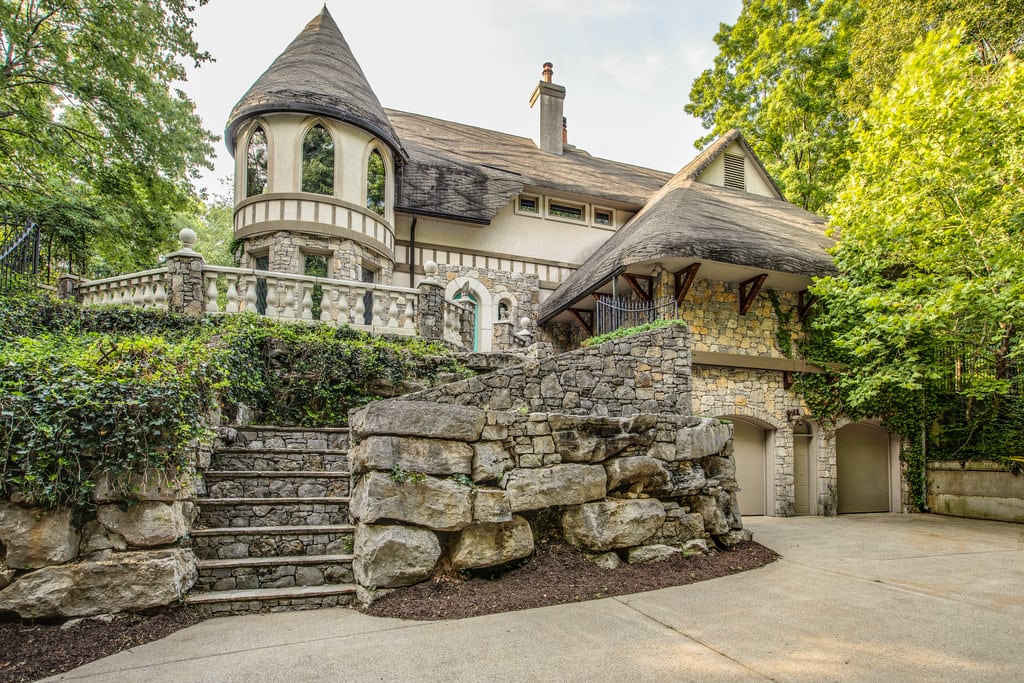 Whimsical stone-and-stucco house with a conical turret, raised terrace, and broad stone steps.