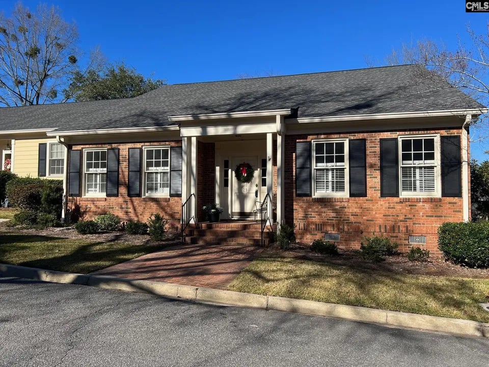 Single-story brick house with black shutters, a covered entrance, and a brick front walkway.