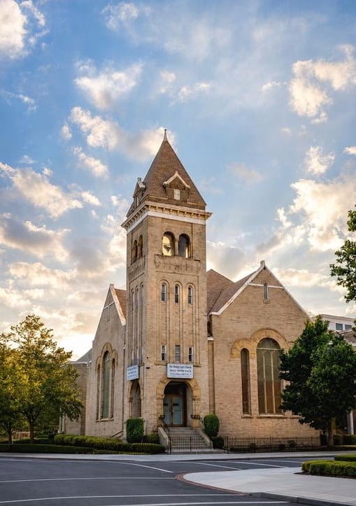 Stone church with a tall central tower, trees, and a partly cloudy sky.