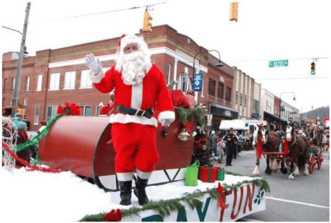 Santa waves from a red sleigh float during a snowy downtown holiday parade.