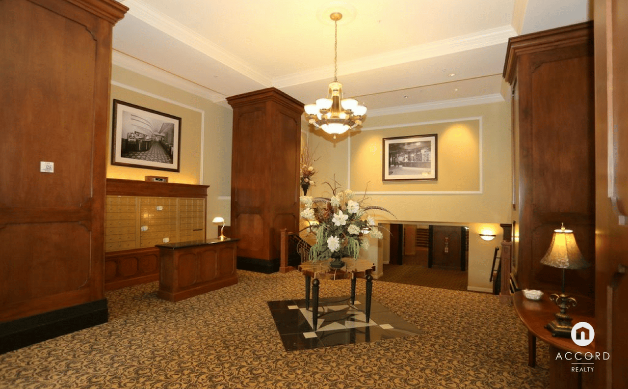 Residential lobby with dark wood paneling, mailboxes, elevator doors, patterned carpet, and a flower arrangement.