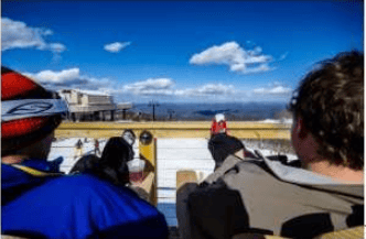 People watch the ski area from a sunny outdoor viewing deck.