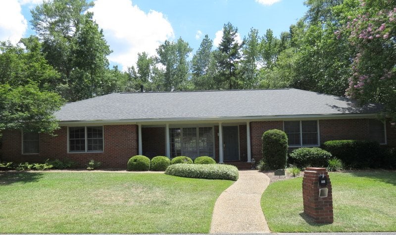 A brick home with a driveway and neatly trimmed bushes in front, showcasing a welcoming residential atmosphere.