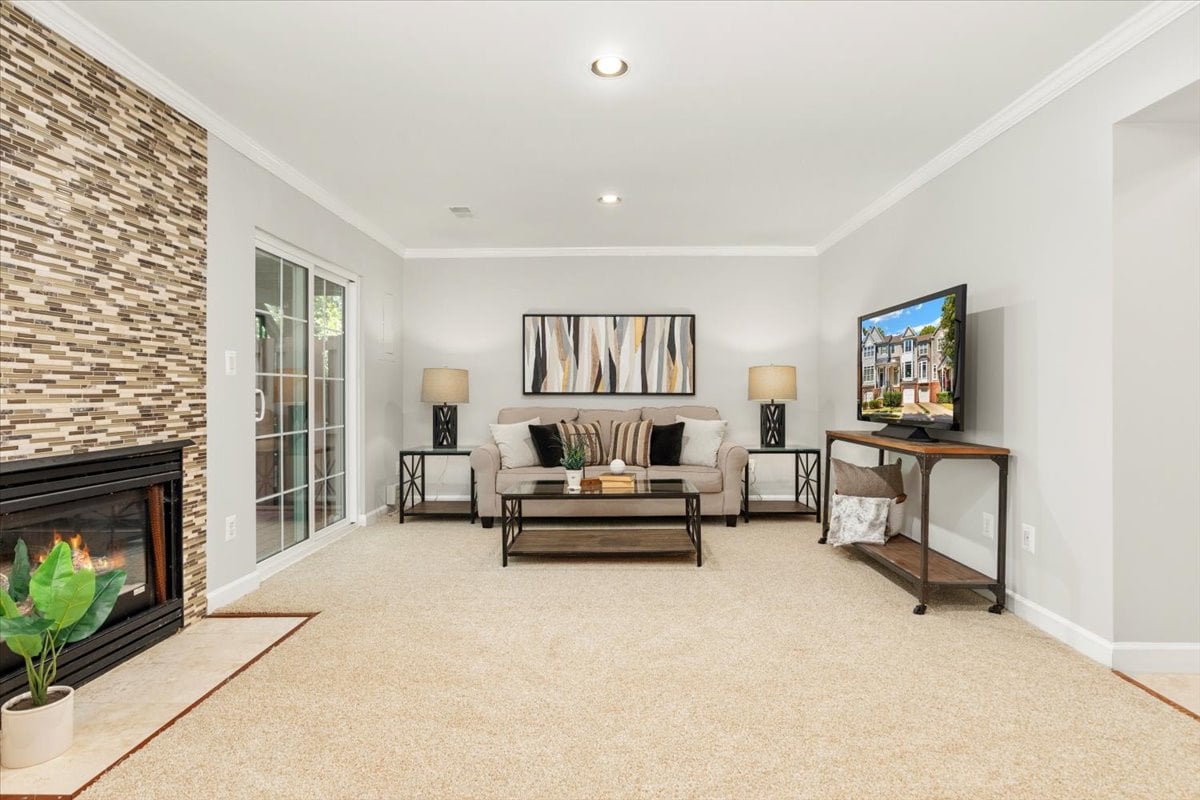 Staged living room with a tiled fireplace, beige sofa, and television.