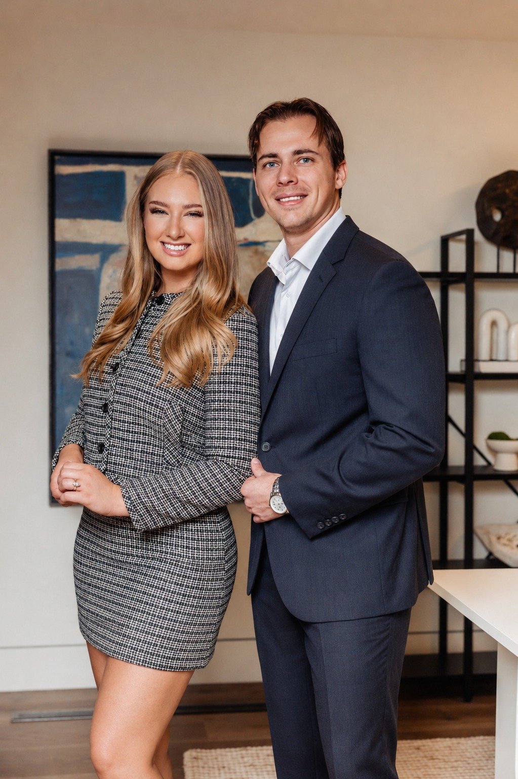 A woman in a patterned dress and a man in a navy suit pose together in an office.