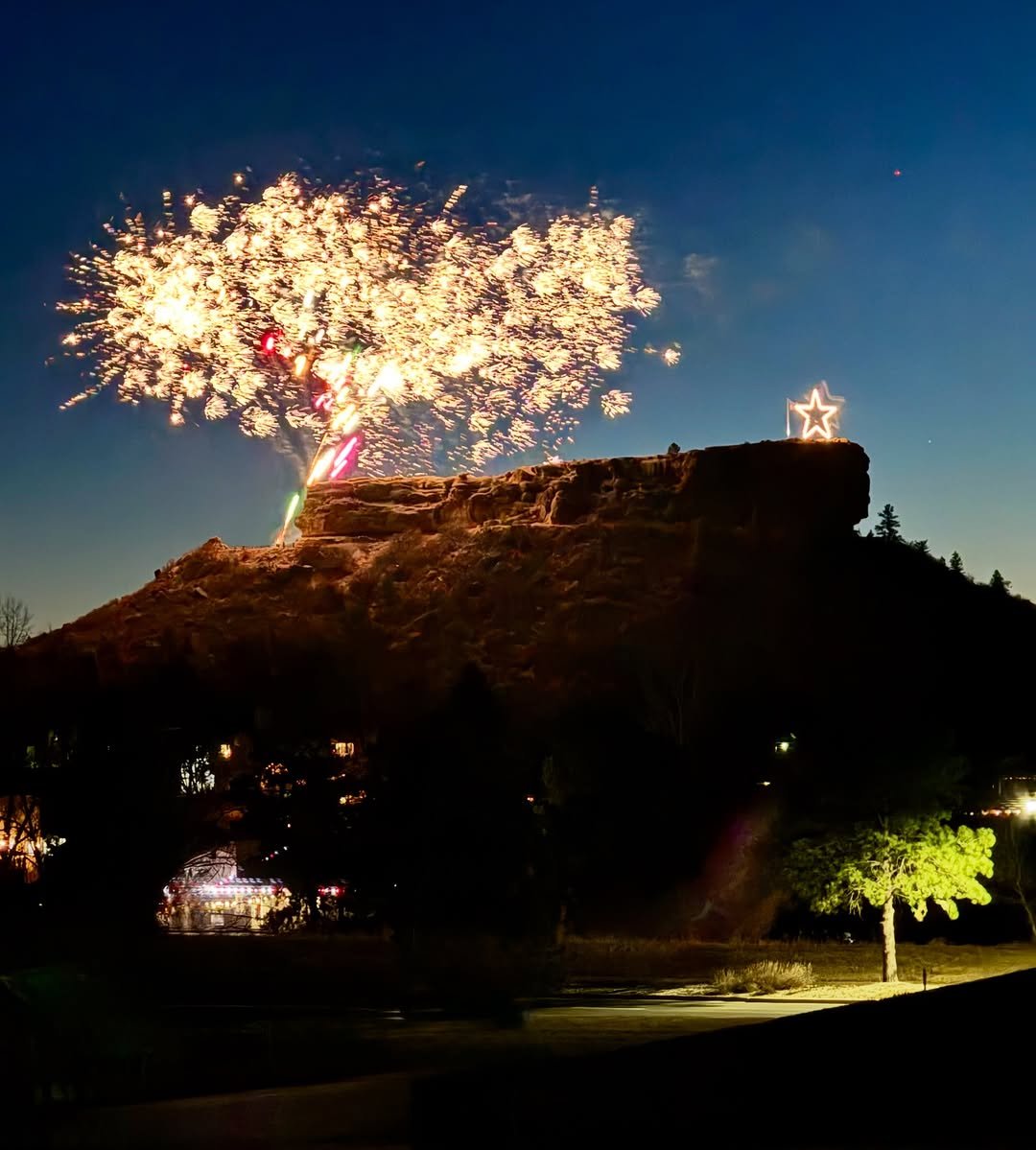 Castle Rock Starlighting 2025 event graphic or photo showing the illuminated star atop Castle Rock, with crowds gathered in downtown, festive decorations, and fireworks lighting up the evening sky.