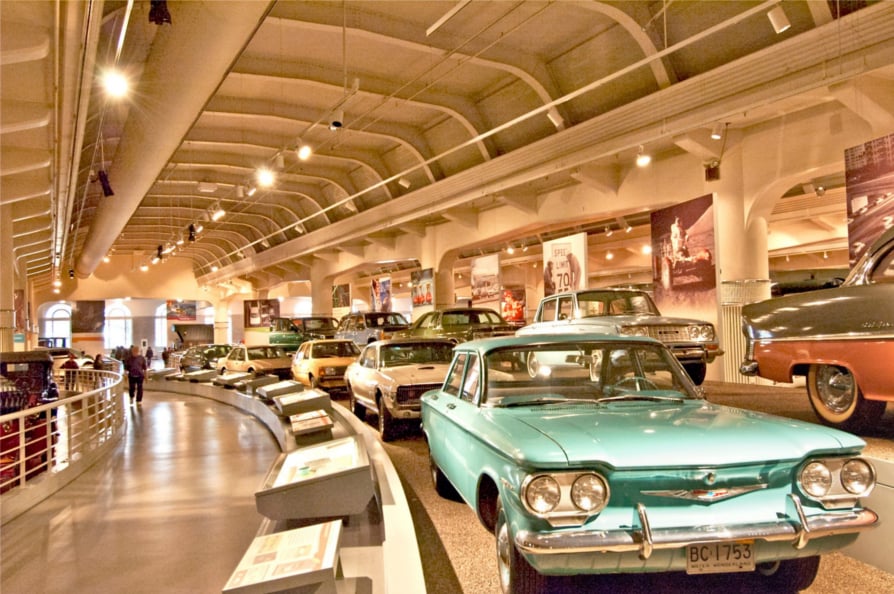 Museum gallery lined with vintage cars, including a turquoise 1960s-era sedan in front.