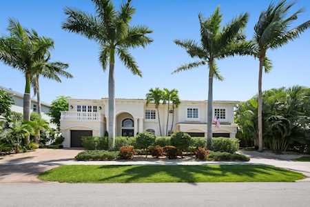 Two-story white home with balconies and an arched entry, framed by tall palms.