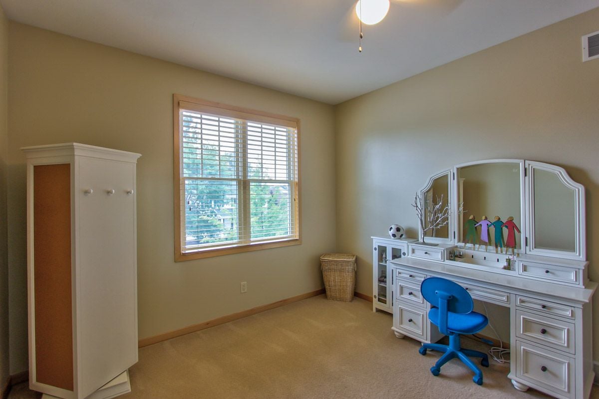 Furnished bedroom with a mirrored vanity desk, blue chair, and large window.