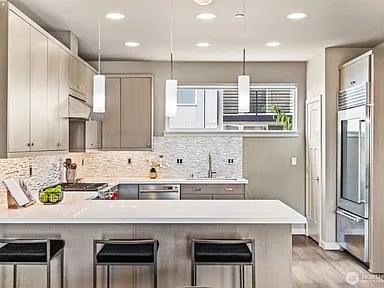 Modern kitchen with a long white island, pale cabinetry, stainless steel appliances, and wood floors.
